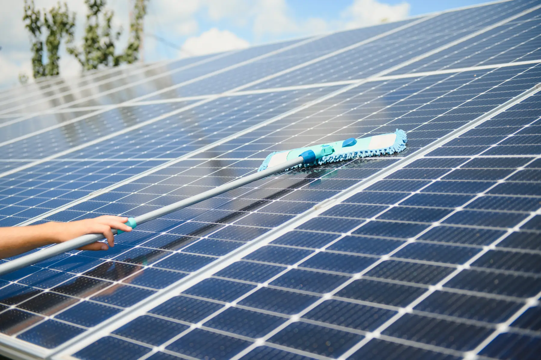 Mopa de microfibra pasando sobre una hilera larga de placas solares azules