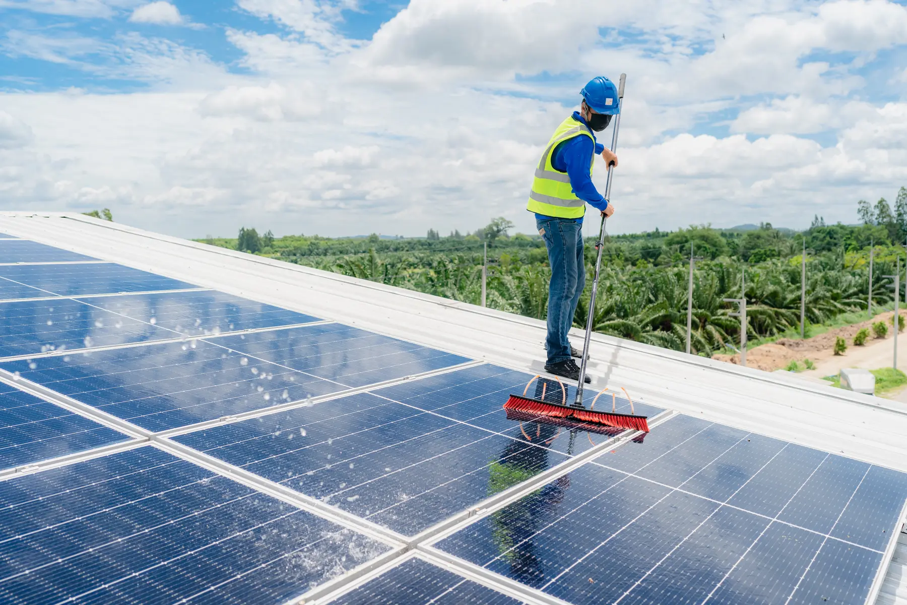 Operario con chaleco reflectante cepillando la cubierta fotovoltaica de una nave