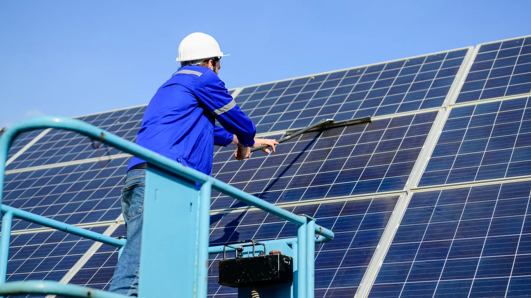 Técnico limpiando placas solares subido a una plataforma elevadora en una instalación grande